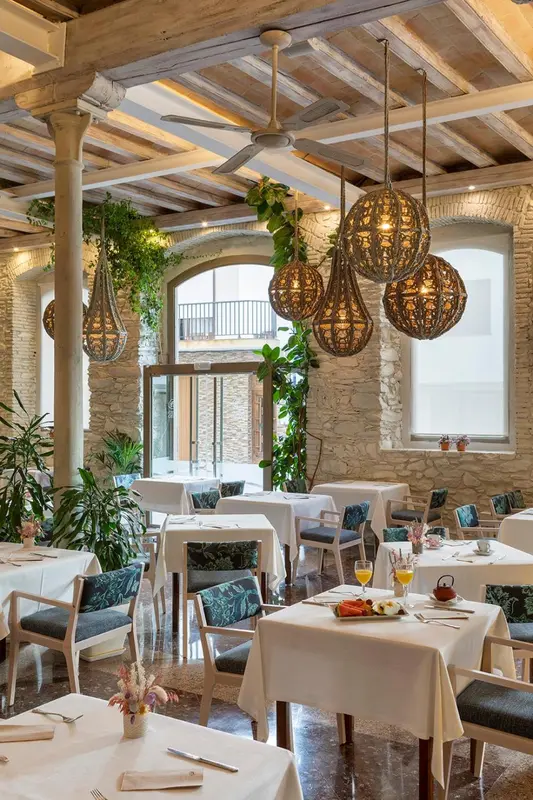 Une salle lumineuse avec des tables nappées et des suspensions décoratives.