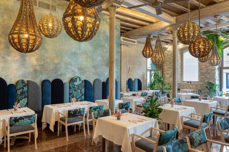 Une salle lumineuse avec des tables nappées et des luminaires décoratifs suspendus au plafond.