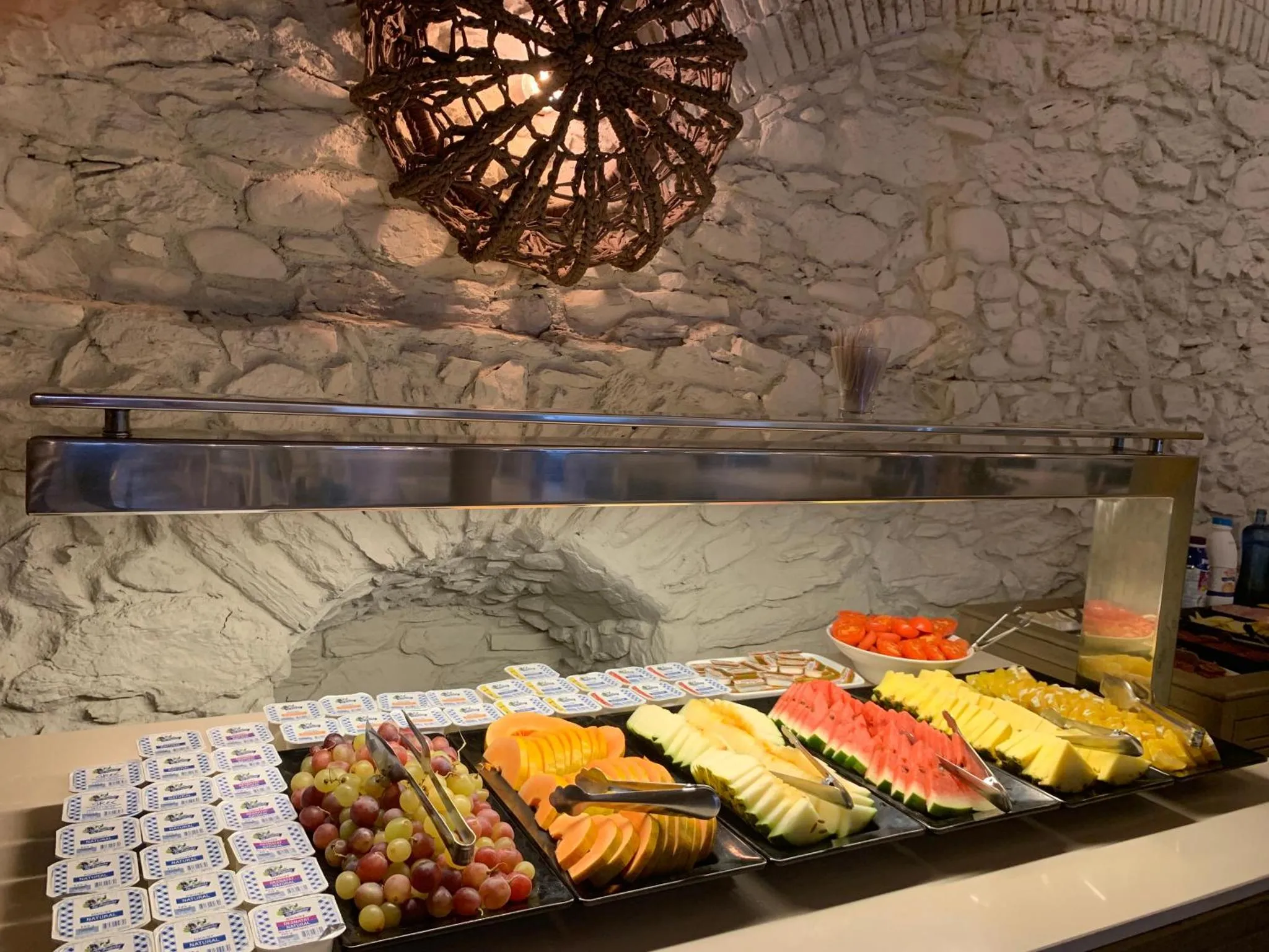 Un buffet propose des fruits frais et des viennoiseries dans un décor mural en pierre.
