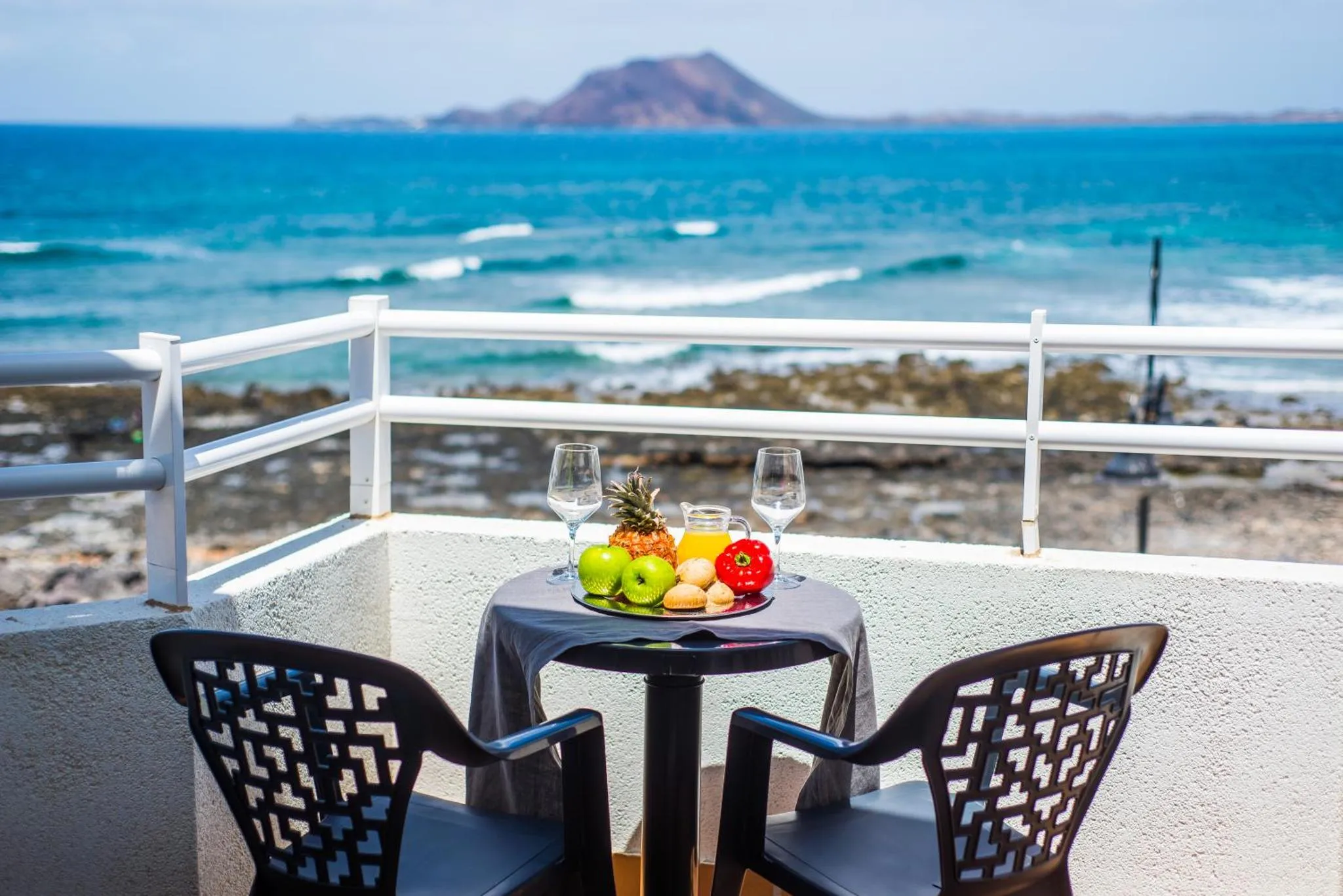 Une table avec des fruits et des verres est mise en scène sur une terrasse avec vue sur la mer.