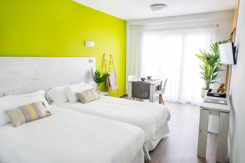 Une chambre lumineuse avec un grand lit recouvert de linge blanc et une table à manger près d'une baie vitrée.