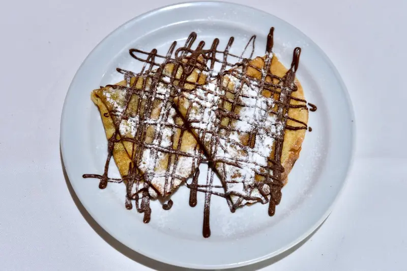 Une crêpe au chocolat saupoudrée de sucre glace est présentée sur une assiette blanche.