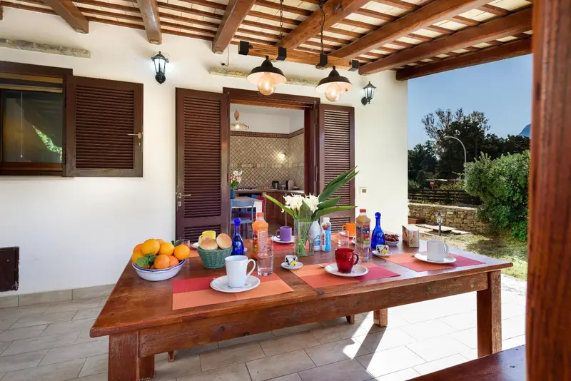 Une table en bois est dressée pour un repas en extérieur, sous une pergola.