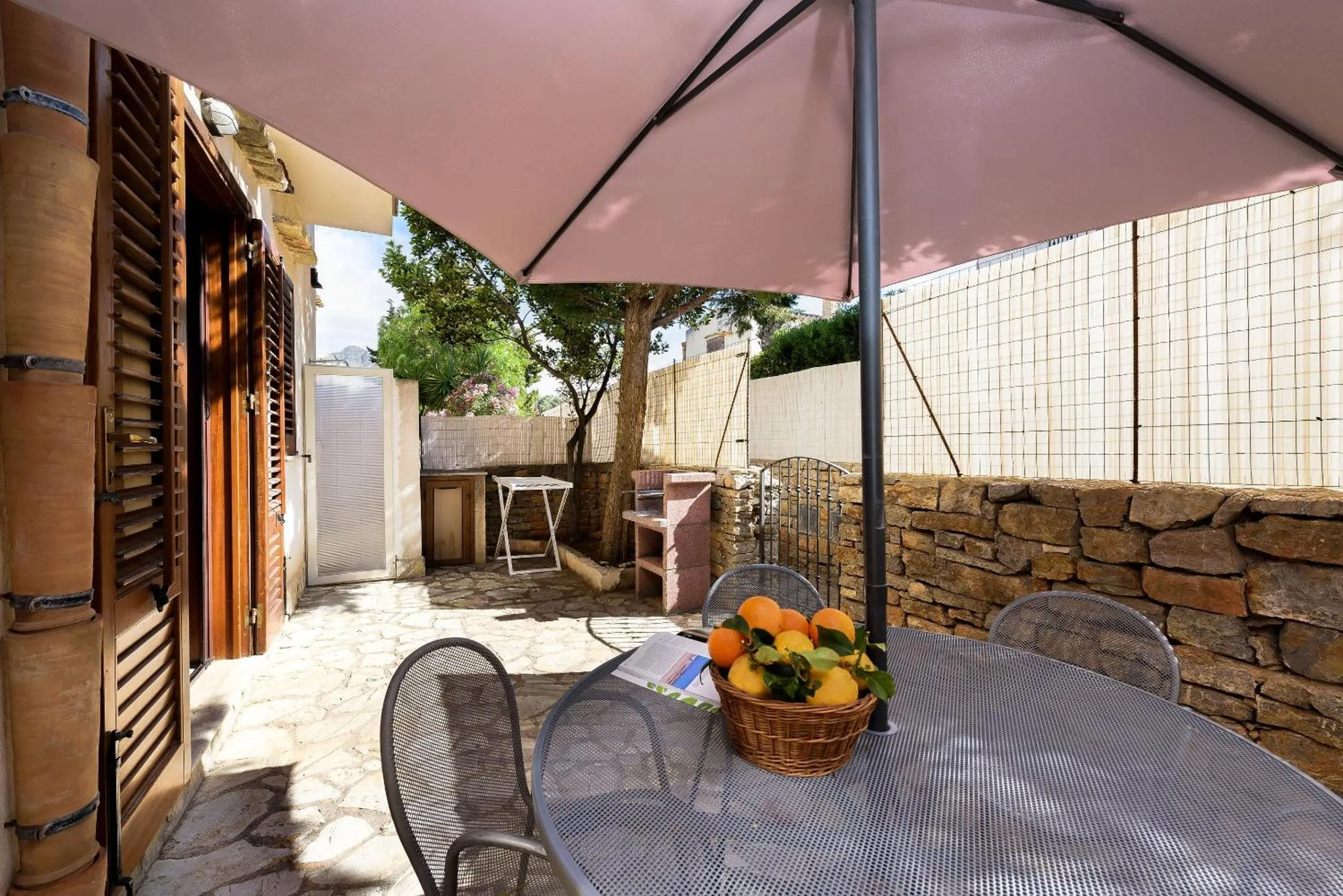 Une table et des chaises en métal se trouvent sur une terrasse pavée ombragée.