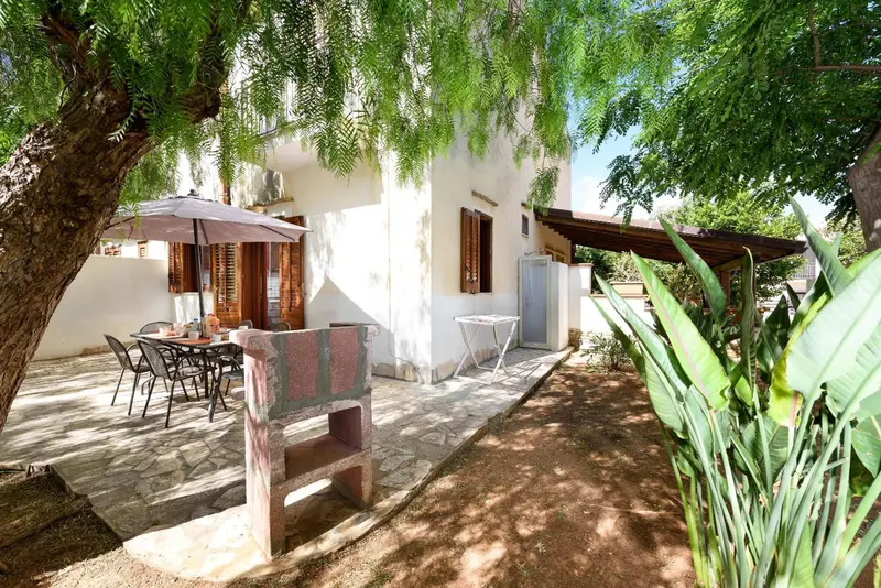 Terrasse ombragée avec mobilier de jardin et barbecue.