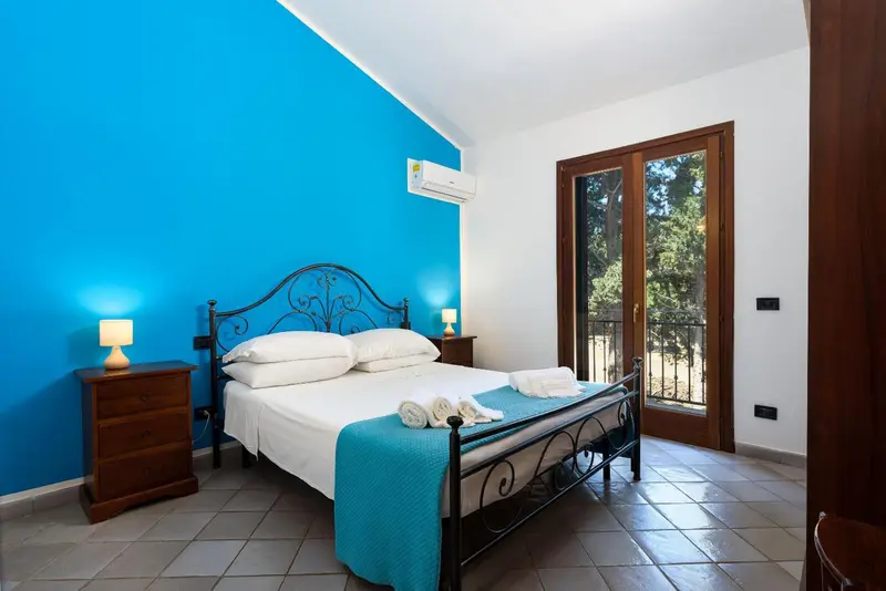 Une chambre lumineuse avec un lit double et une porte-fenêtre donnant sur l'extérieur.