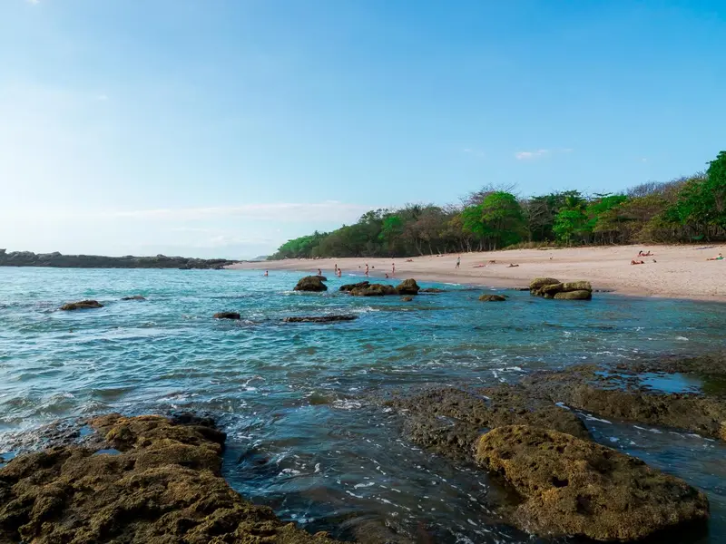 Une plage de sable clair bordée d'une eau turquoise et de rochers.