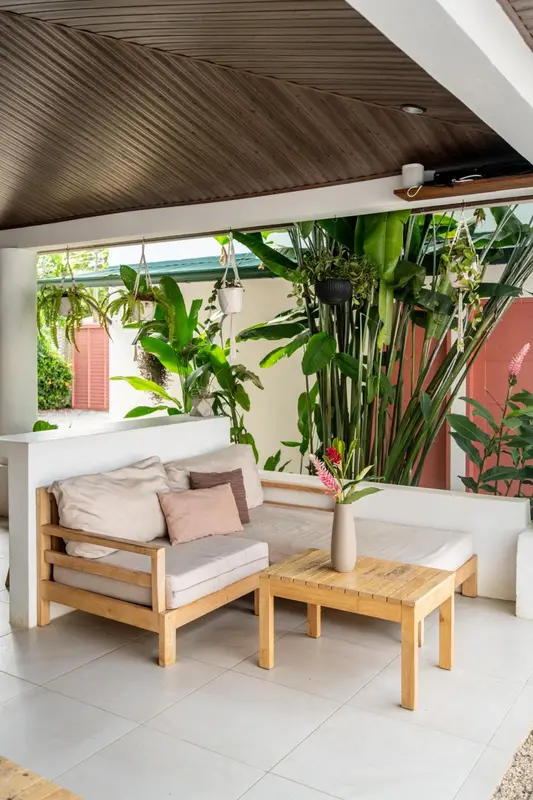 Un coin salon extérieur avec canapé et table basse se trouve sous un toit végétalisé.