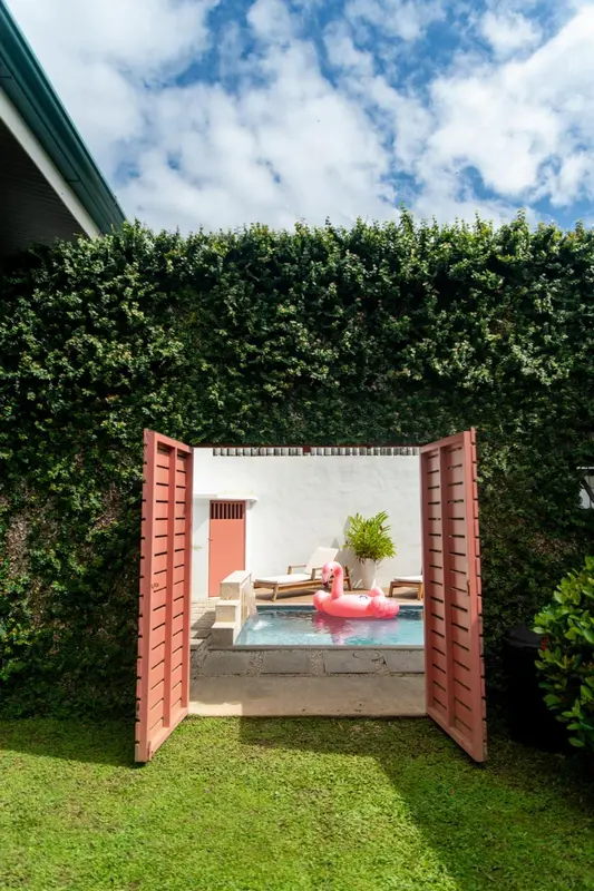 Une petite piscine rectangulaire avec un flamant rose gonflable est visible à travers une ouverture dans un mur.