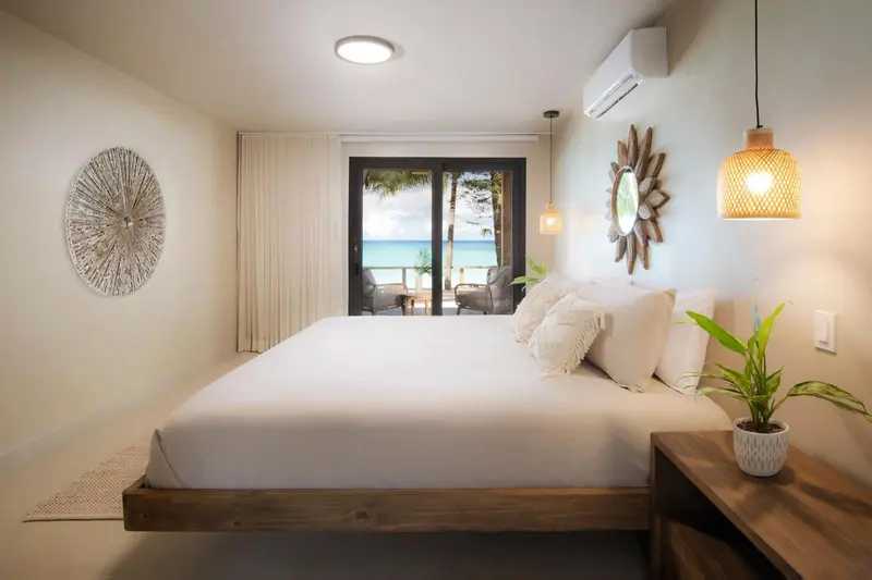 Une chambre lumineuse avec un grand lit face à une baie vitrée donnant sur la mer.
