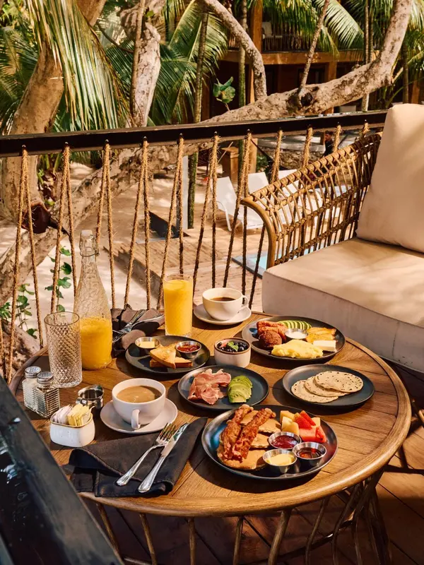 Une table ronde en bois est dressée avec un petit-déjeuner copieux sur une terrasse.