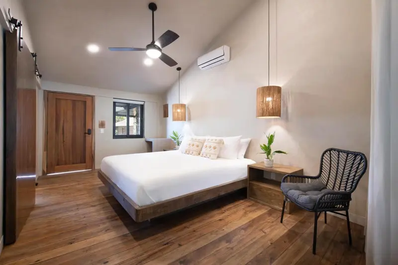 Une chambre lumineuse avec un grand lit et un fauteuil en rotin.