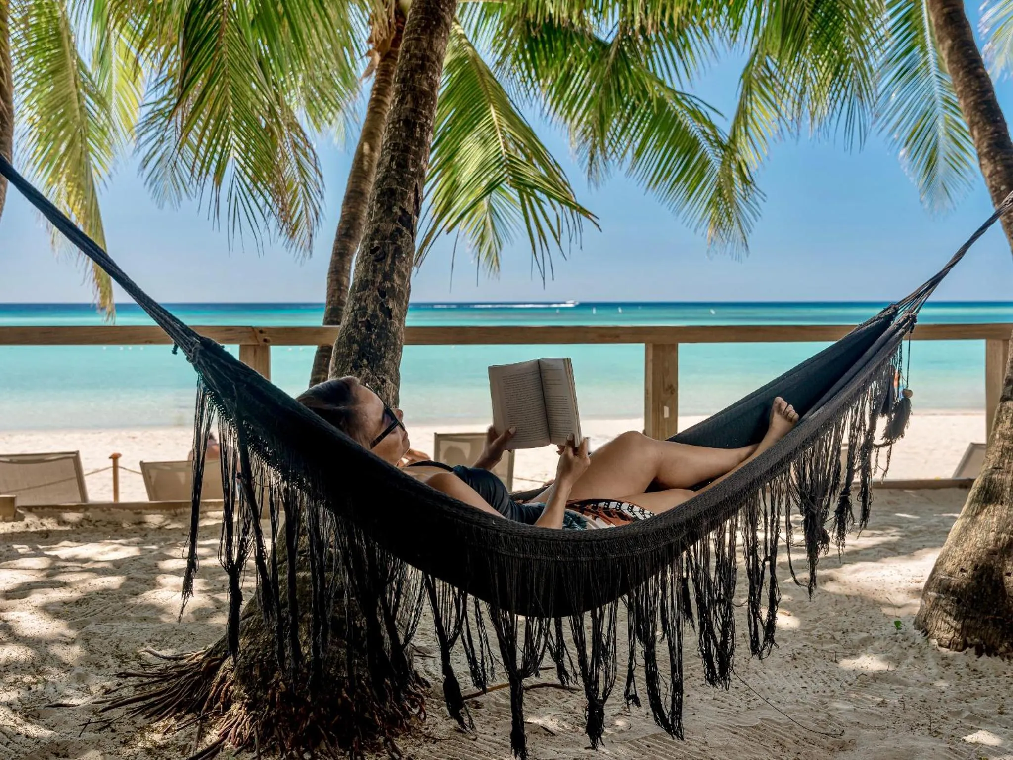 Une personne se détend dans un hamac sur une plage de sable blanc.