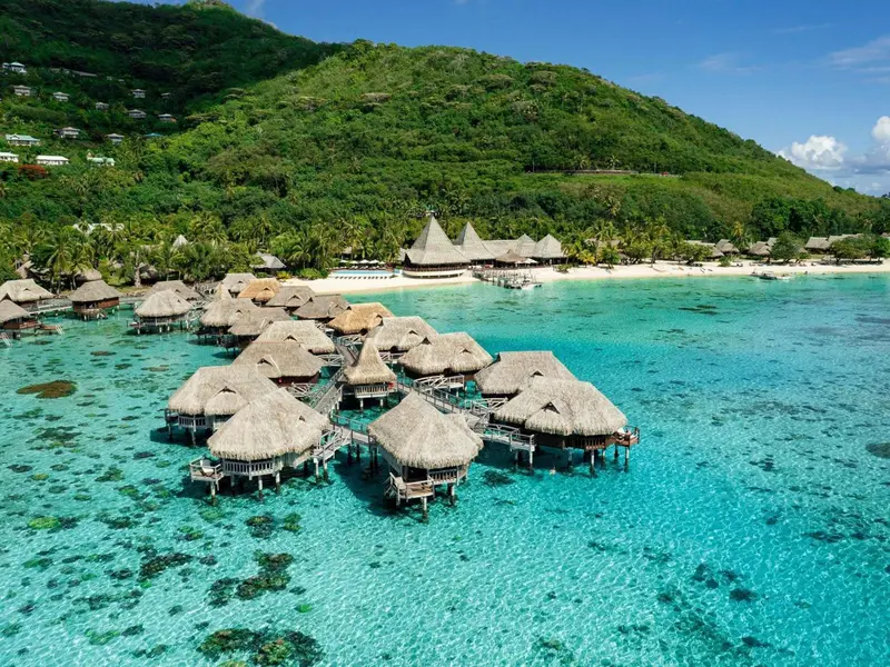 Vue aérienne d'un complexe hôtelier sur pilotis au milieu d'un lagon turquoise.