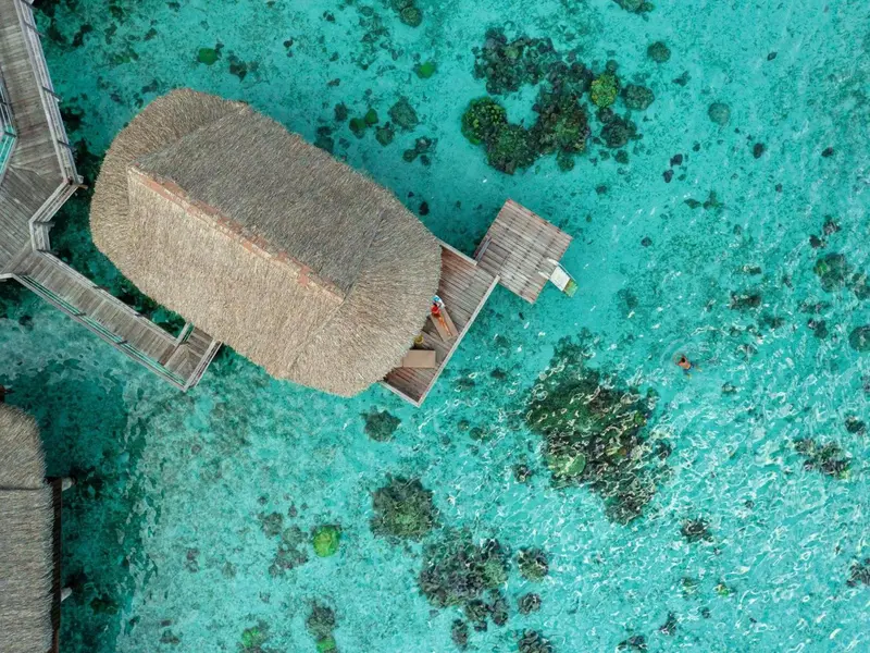 Vue aérienne d'un bungalow sur pilotis au-dessus d'un lagon turquoise.