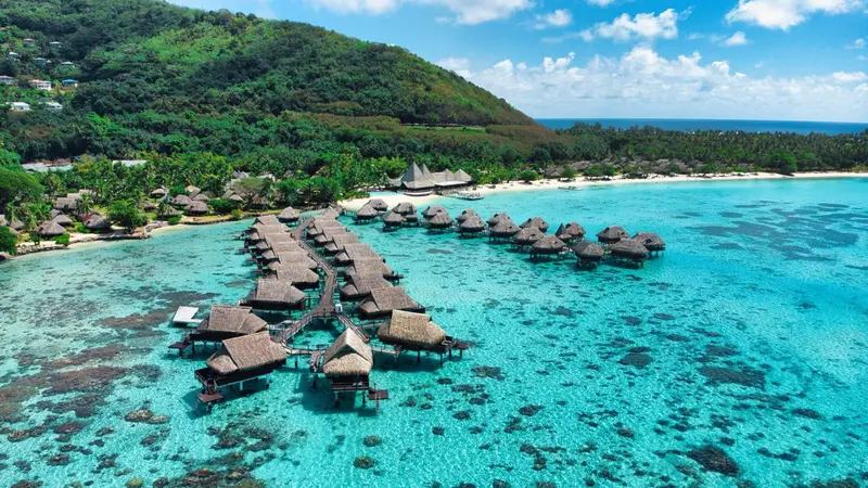 Vue aérienne d'un ensemble de bungalows sur pilotis dans une lagune turquoise.
