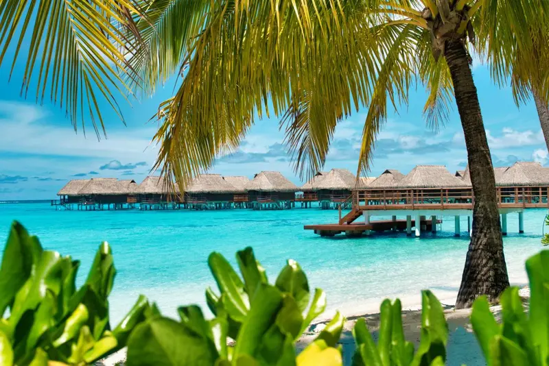 Des bungalows sur pilotis bordent une eau turquoise sous un ciel bleu.