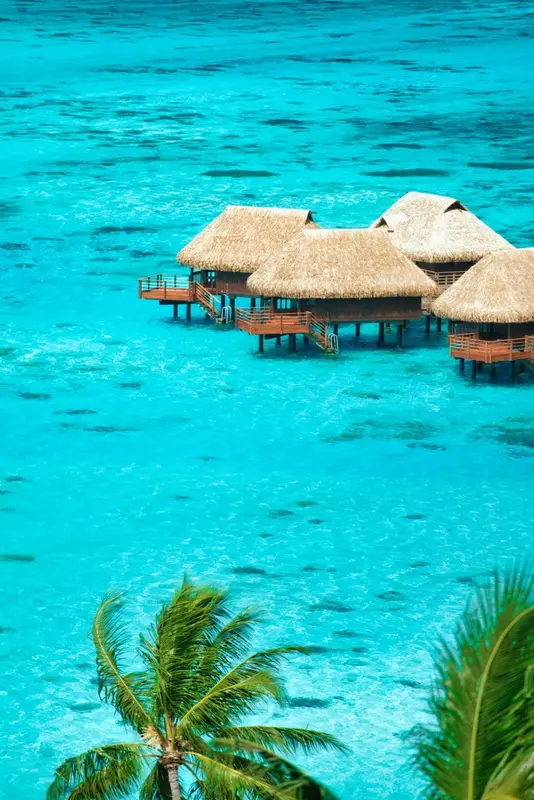 Cabanes sur pilotis au-dessus d'une eau turquoise claire.