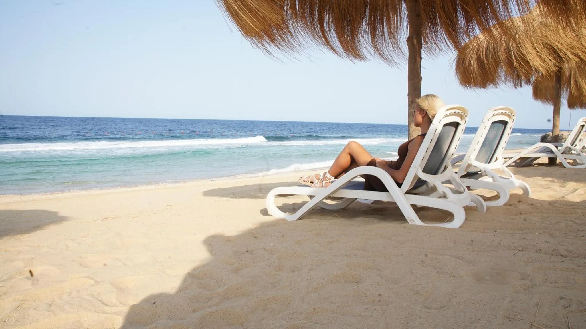 Une femme se relaxe sur des transats sur une plage de sable fin.