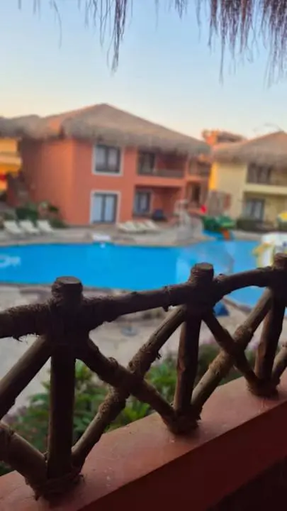 Vue sur une piscine et des bâtiments avec toits de chaume depuis une terrasse.