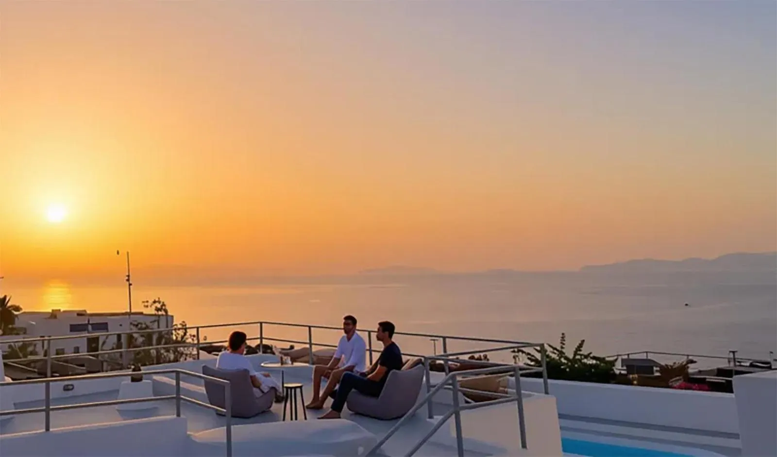 Des personnes se détendent sur une terrasse avec vue sur la mer au coucher du soleil.