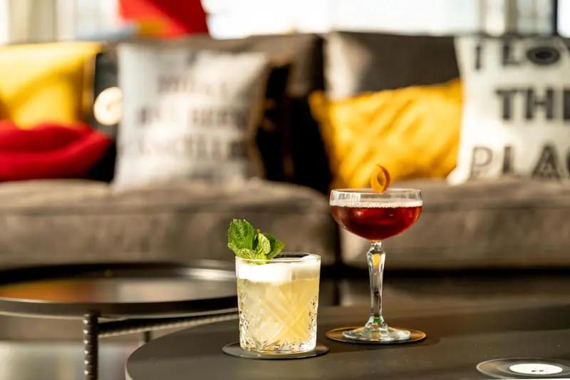 Deux cocktails colorés reposent sur des tables basses devant des coussins décoratifs.