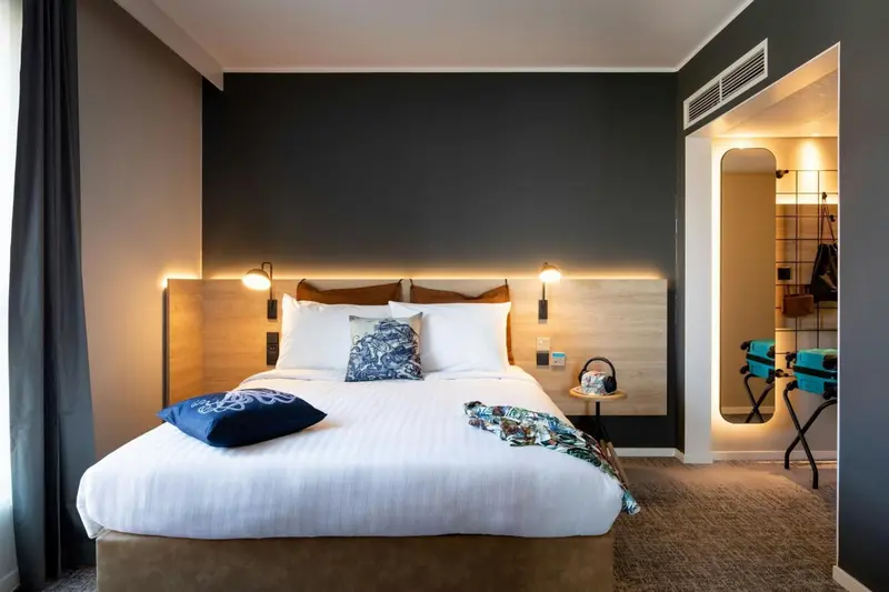 Une chambre avec un grand lit recouvert d'une couette blanche et de coussins.