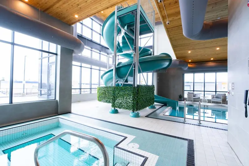 Un toboggan aquatique vert descend vers une piscine intérieure lumineuse.