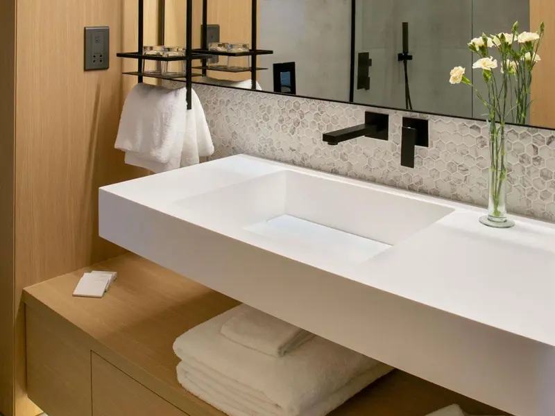 Un lavabo blanc moderne avec un grand miroir et des serviettes pliées.