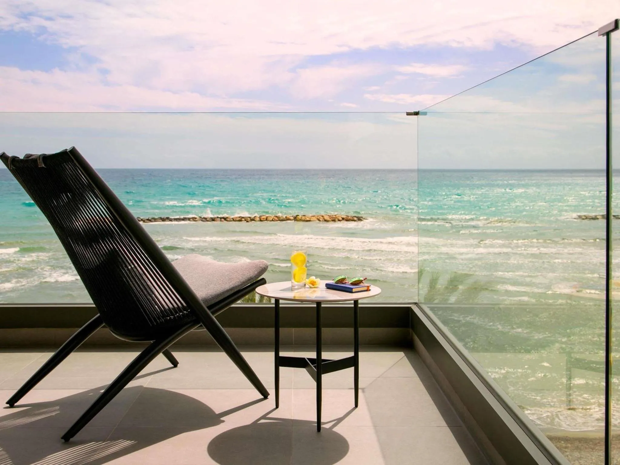 Une chaise longue et une table avec des boissons sont posées sur une terrasse avec vue sur la mer.