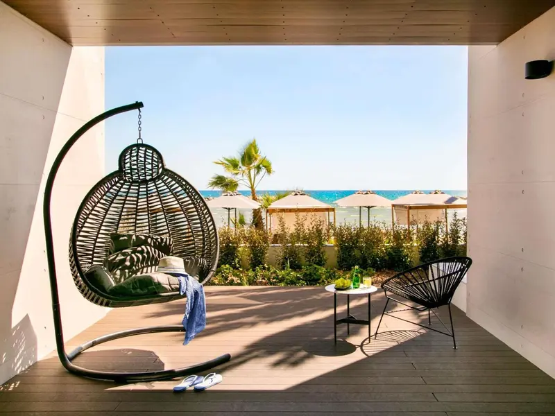 Un fauteuil suspendu en osier se trouve sur une terrasse en bois avec vue sur la mer.