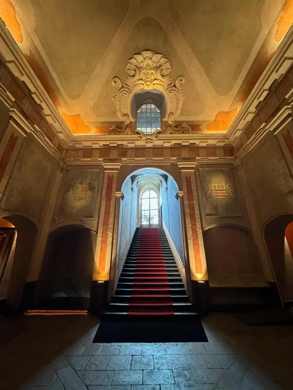 Un escalier en pierre rouge mène à un étage supérieur dans un hall décoré.
