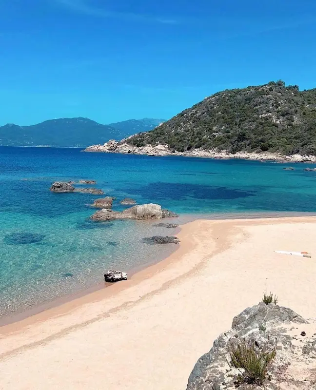 Une plage de sable fin borde une eau turquoise sous un ciel bleu.