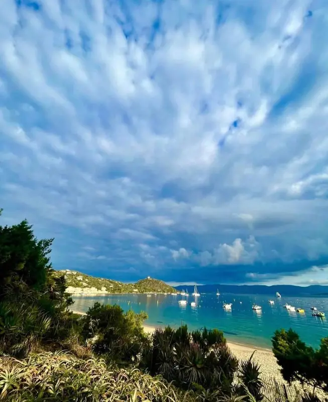 Une plage de sable fin bordée d'une eau turquoise sous un ciel nuageux.