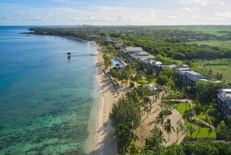 Vue aérienne d'une plage bordée de bâtiments et de végétation luxuriante.