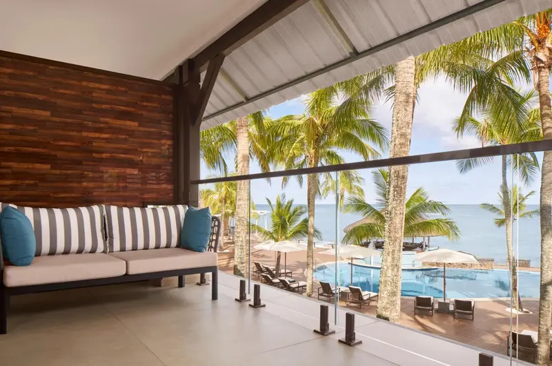 Canapé rayé bleu et blanc sur une terrasse ouverte sur une piscine et la mer.