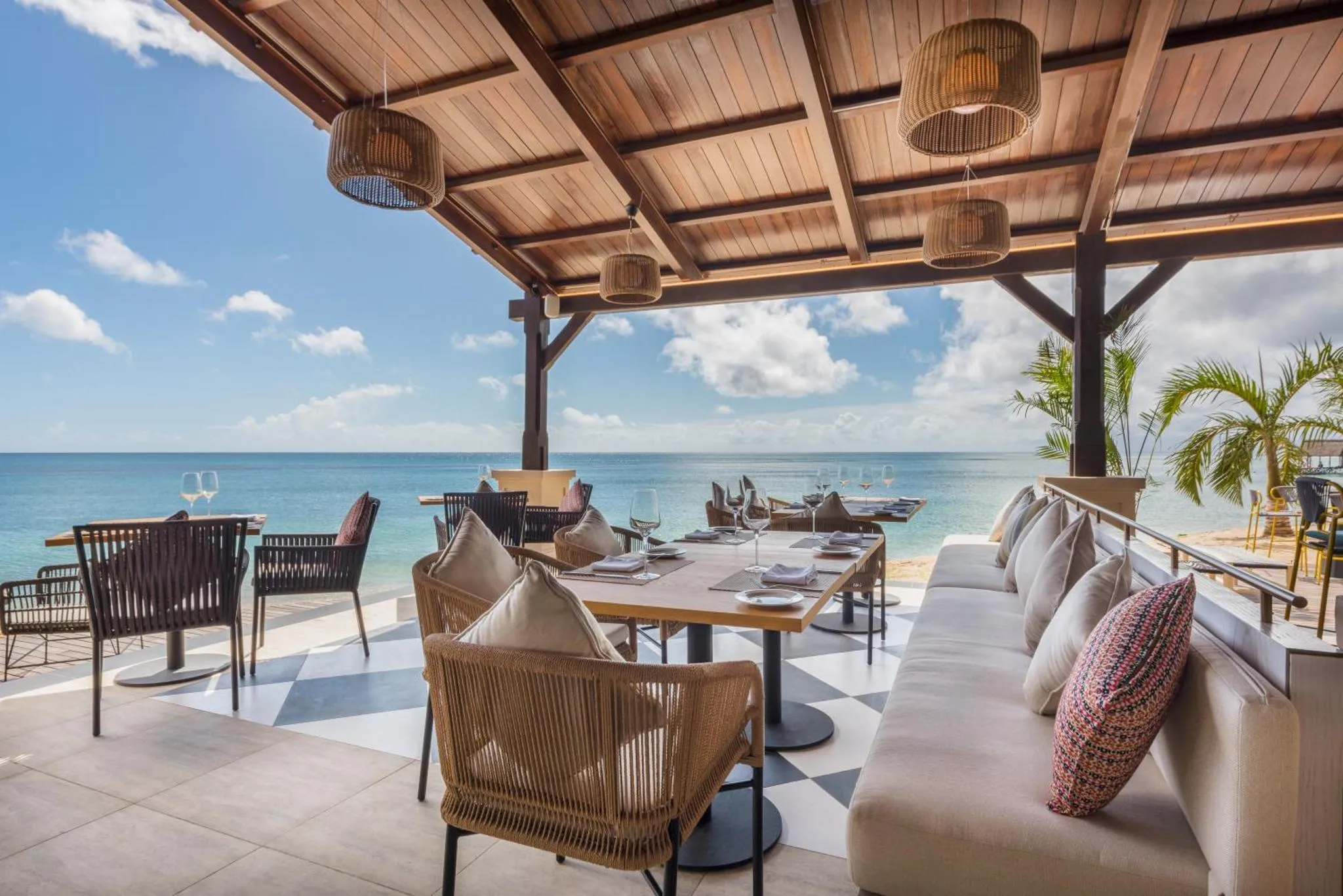 Terrasse ombragée avec tables et canapés face à la mer.