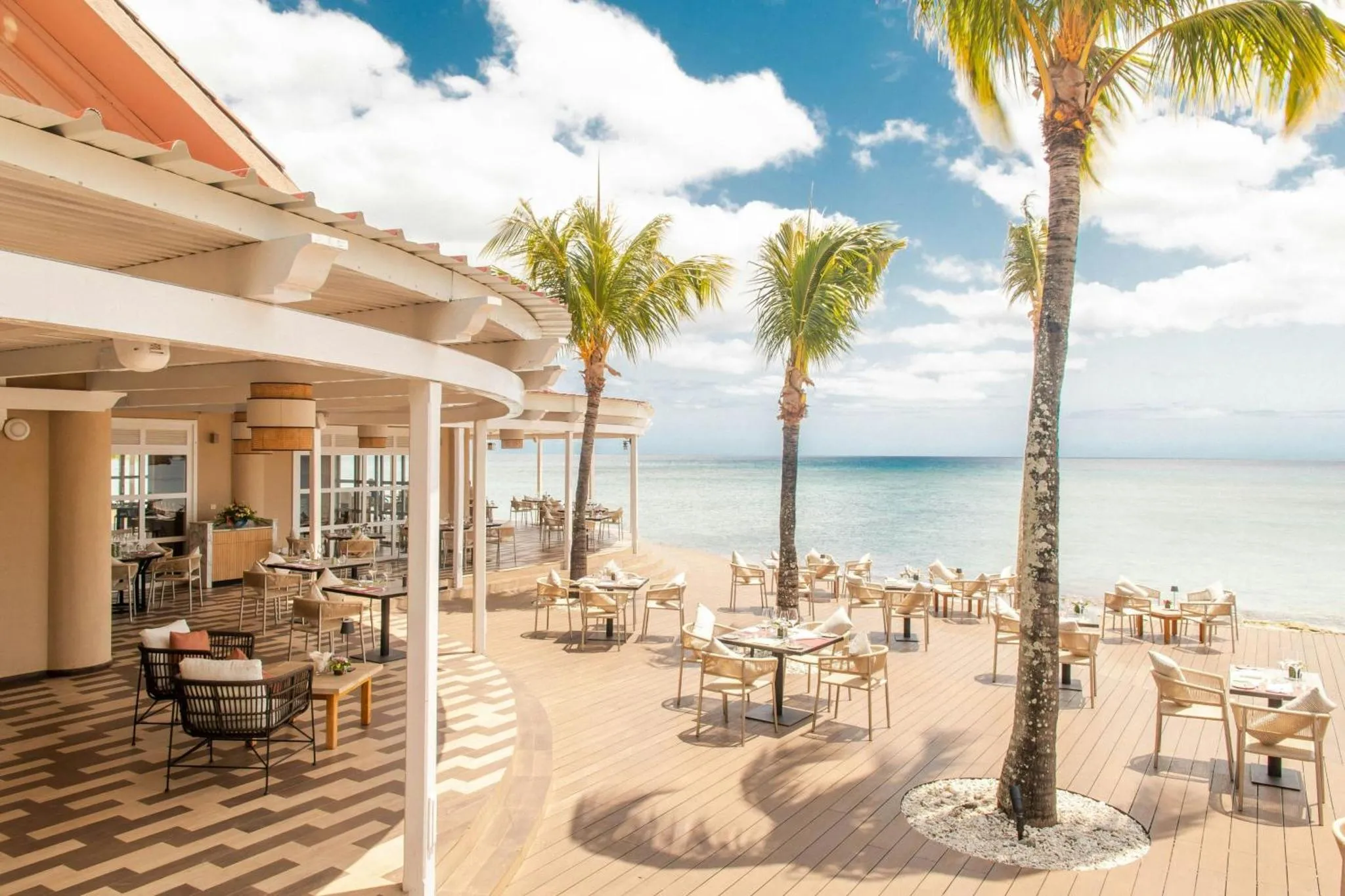 Terrasse ombragée avec tables et chaises donnant sur la mer.