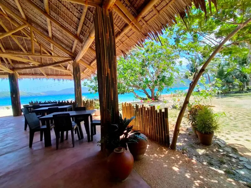 Une salle à manger en plein air s'ouvre sur une plage ensoleillée.