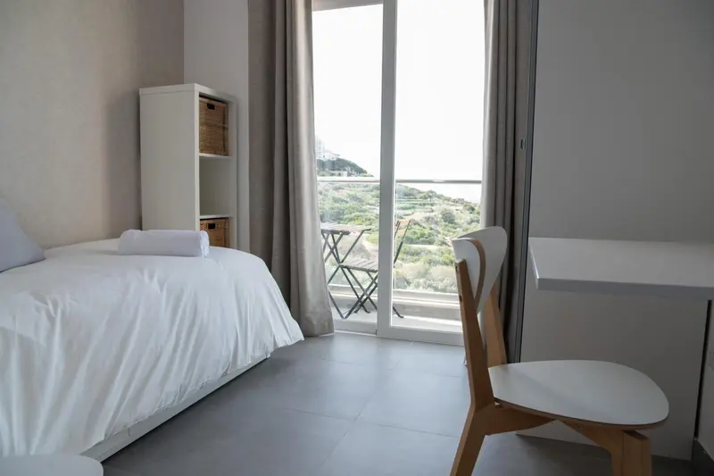 Une chambre lumineuse avec un lit simple et une vue sur la mer.