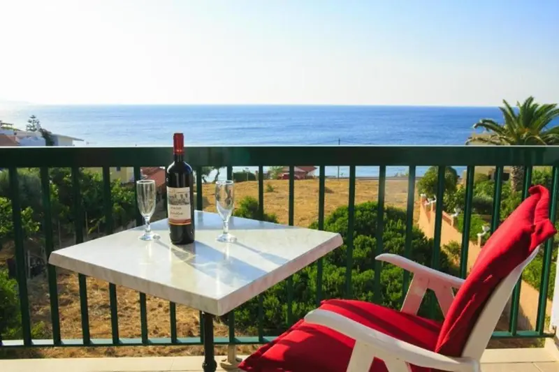 Une table avec une bouteille de vin et des verres sur une terrasse ensoleillée avec vue sur la mer.