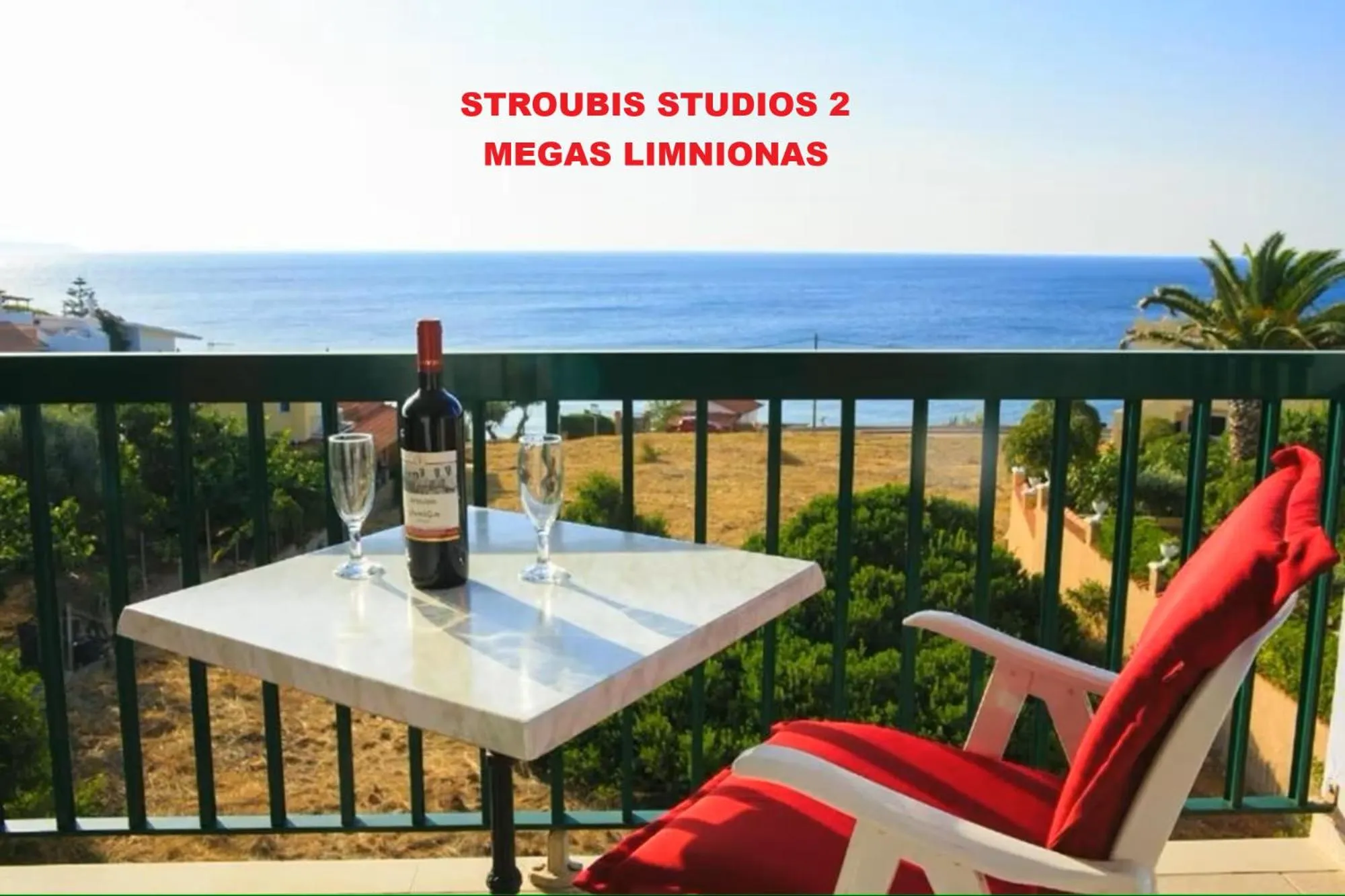 Une table avec une bouteille de vin et deux verres sur une terrasse ensoleillée avec vue sur la mer.
