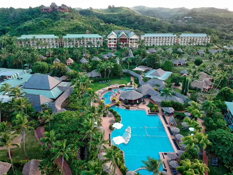 Vue aérienne d'un complexe hôtelier tropical avec piscine et végétation luxuriante.