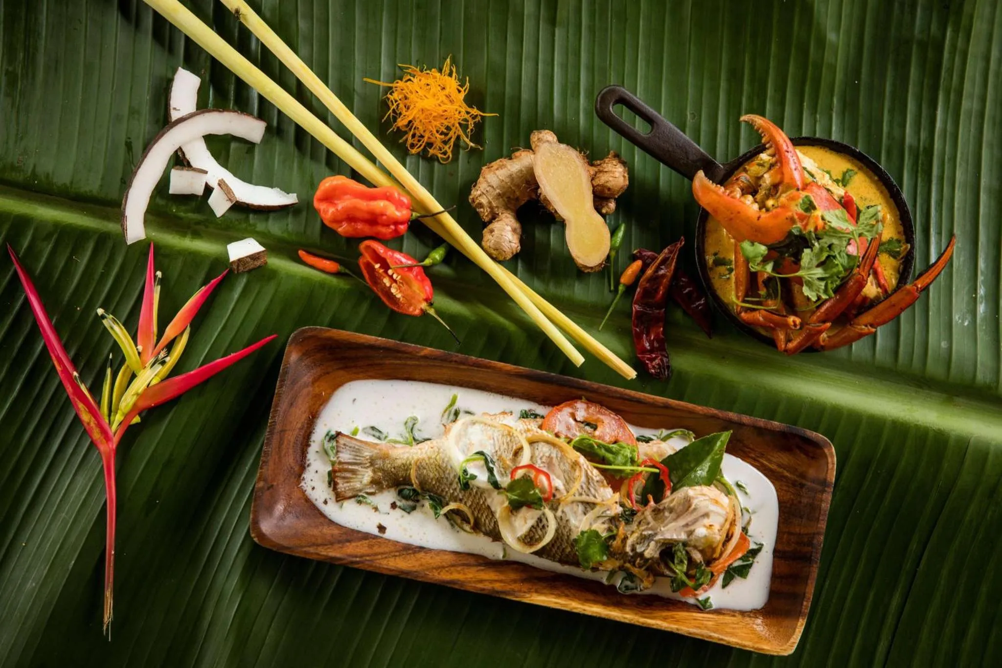 Présentation de plats de poisson et de fruits exotiques sur des feuilles de bananier.