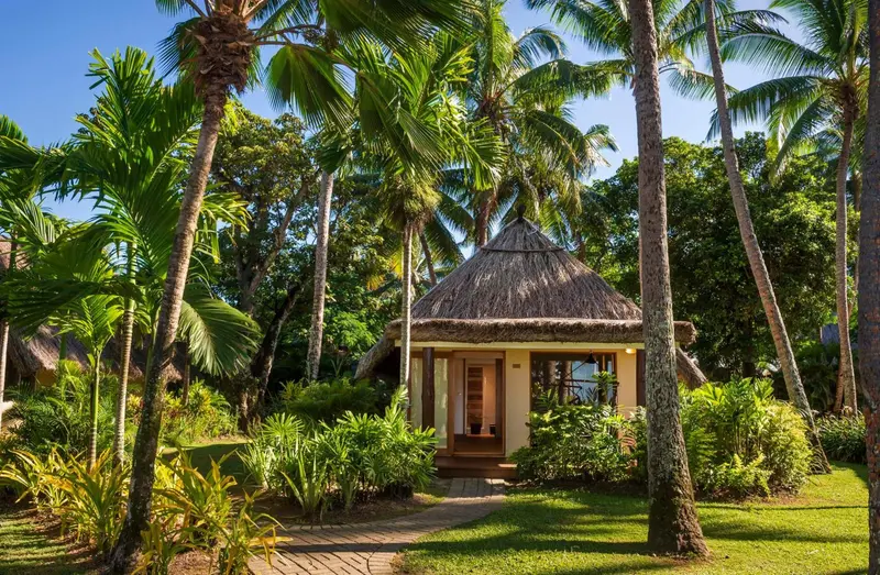 Un bungalow de style tropical avec un toit de chaume se trouve au milieu d'une végétation luxuriante.