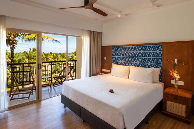 Une chambre lumineuse avec un grand lit et un balcon donnant sur une végétation luxuriante.