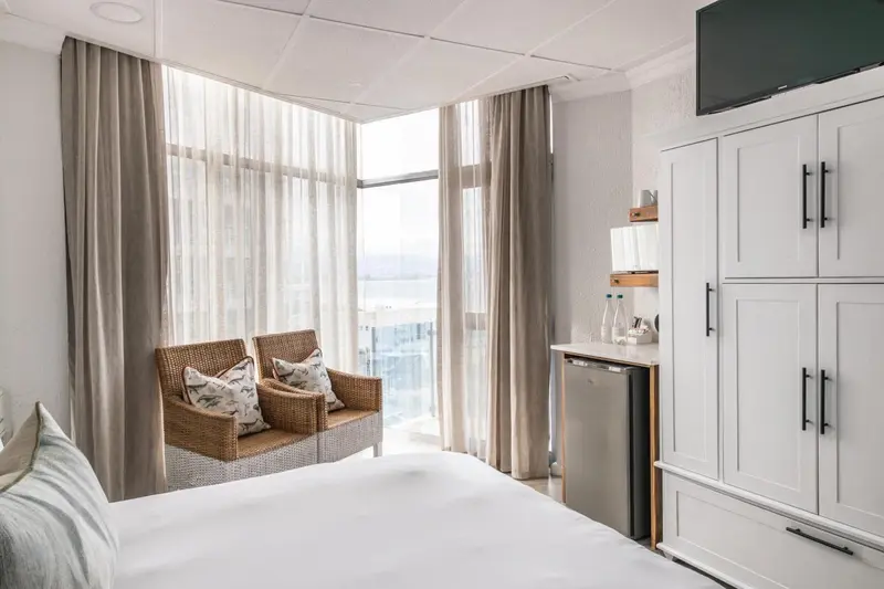 Une chambre lumineuse avec un coin salon près d'une fenêtre donnant sur la mer.