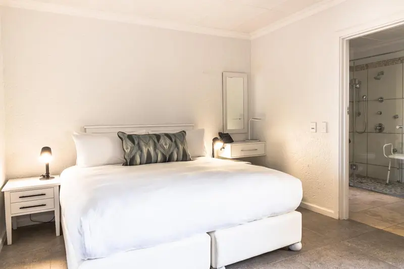 Une chambre lumineuse avec un lit blanc et une salle de bain vitrée.