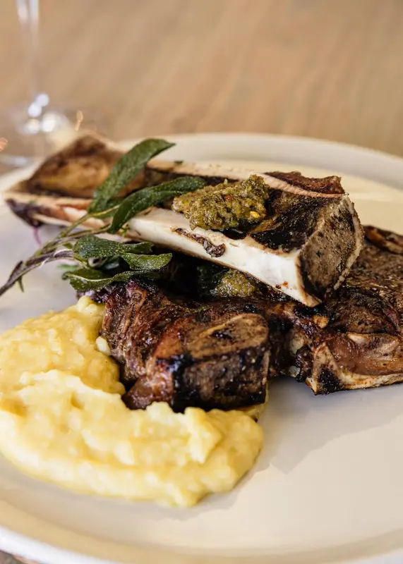 Assiette de viande grillée accompagnée d'une purée et d'une sauce verte.