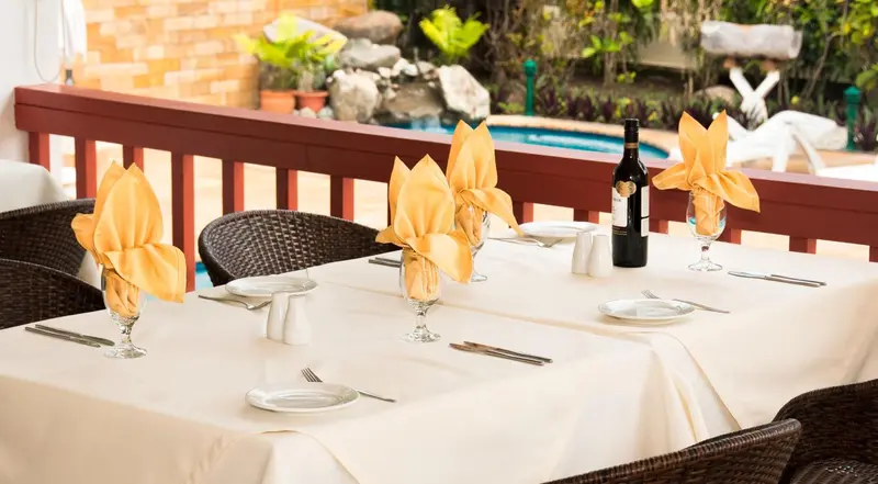 Une table dressée avec des couverts et une bouteille de vin près d'une piscine.
